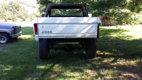 1978 Ford Bronco - Rear view of a white 1978 Ford Bronco, showing its tailgate and rear axle, with another vehicle to its left.