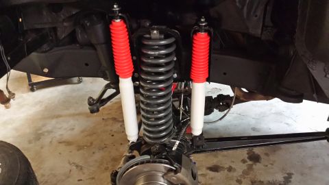 1978 Ford Bronco - Close-up view of the front suspension system, red and white shock absorbers and large coil springs.