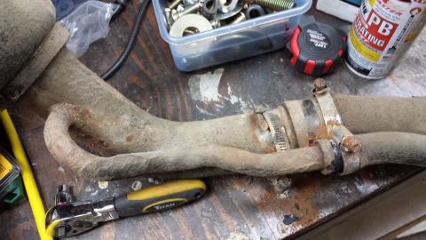 1978 Ford Bronco - Exhaust pipe section with clamps and a ratchet tool on a wooden surface.