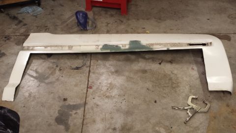 1978 Ford Bronco - A white car fender part is shown lying on a concrete floor, with some green filler visible on its surface.
