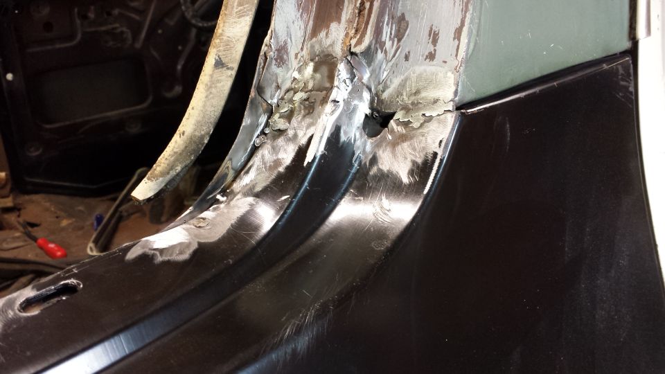 Close-up of rusted metal panel repair with visible welds and grinding marks
