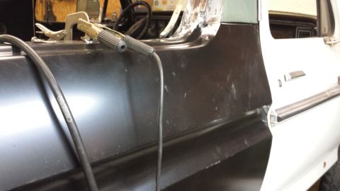 1978 Ford Bronco - Close-up of a vehicle's side panel being worked on, with welding equipment attached.