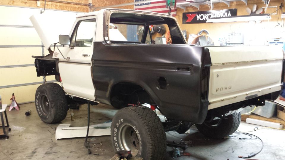 Ford Bronco body on lift, hood open, dark primer on rear quarter panel