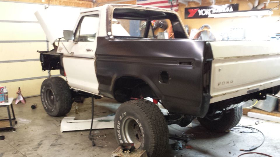 White and dark brown 1978 Ford Bronco undergoing repairs, viewed from the rear three-quarter angle