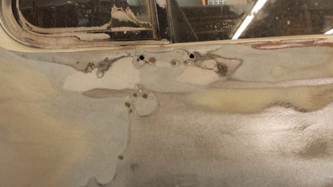 1978 Ford Bronco - Close-up of bodywork and primer on a vehicle door, showing areas of repair and two screw holes.