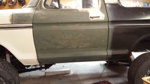 1978 Ford Bronco - Side view of a 1978 Ford Bronco with bodywork in progress, primer on front section, dark paint on rear.