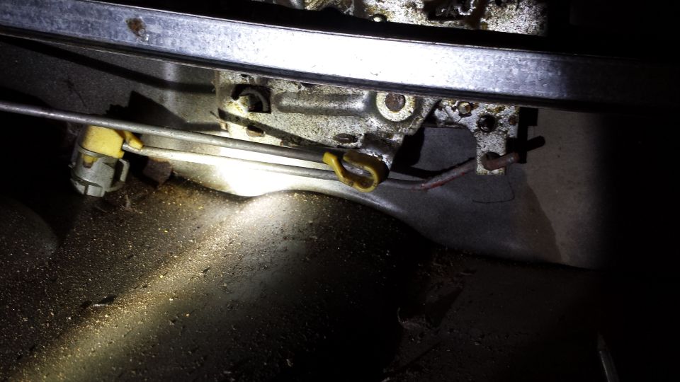 Close-up of a car's interior door latch mechanism with cables and yellow plastic parts