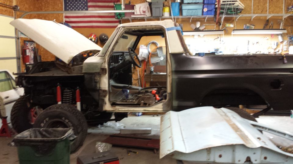Ford F-Series truck in garage, hood up, doors open, undergoing repairs