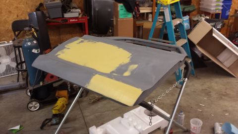 1978 Ford Bronco - A car door, prepped with yellow primer, sits on a stand in a workshop.