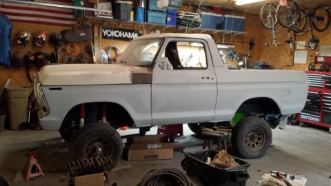 1978 Ford Bronco - A 1978 Ford Bronco is shown in a garage, appearing to be in the process of restoration with its body primed and suspension exposed.