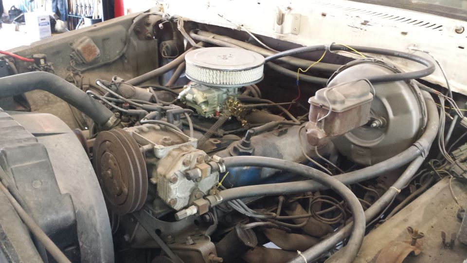 Engine bay with V8 engine, carburetor, and air filter. Visible AC compressor and brake booster