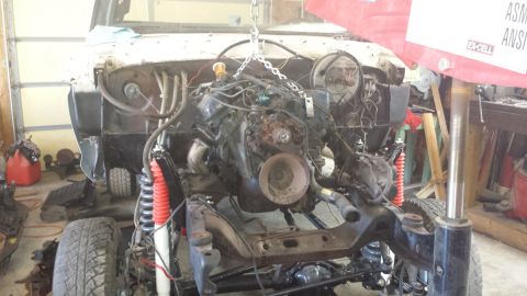 1978 Ford Bronco - The engine is suspended by a chain hoist, with the vehicle's chassis and suspension visible below.
