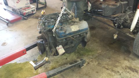 1978 Ford Bronco - Engine removed from a vehicle and suspended by an engine hoist in a garage setting.