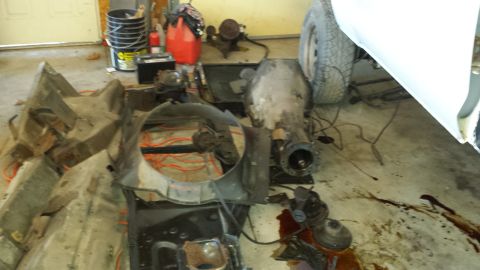 1978 Ford Bronco - Vehicle parts are disassembled and spread across a garage floor, with a transmission and fan shroud prominently visible.