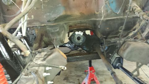 1978 Ford Bronco - Underside view of vehicle frame and drivetrain components, supported by a red jack stand.