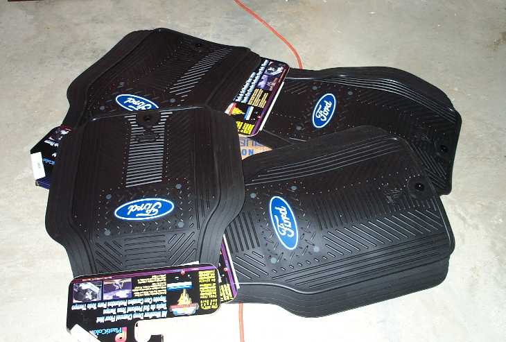Black Ford rubber floor mats with logos and retail tags on a concrete floor