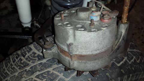 1978 Ford Bronco - This is a close-up view of a vehicle's alternator, resting on a tire with part of a shock absorber visible.