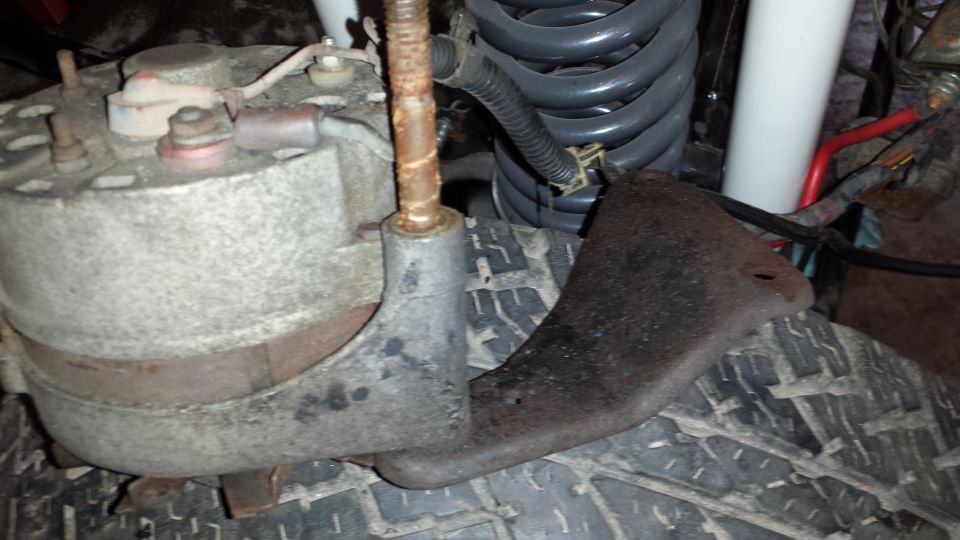 Alternator and rusty bracket mounted near a tire and coil spring