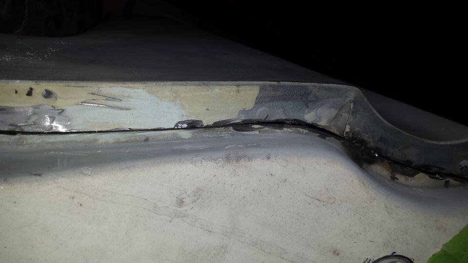 Close-up of a dented and repaired vehicle body panel with visible welds and primer