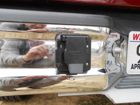1992 Ford Bronco - A close-up view of a trailer hitch connector attached to a vehicle's chrome bumper.