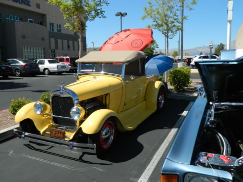 1979 Ford Bronco - A yellow 1928 Ford Model A convertible is parked in a lot, with umbrellas providing shade.