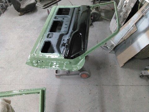 1960 Ford Ranchero - A car door is mounted on a stand, likely for restoration or painting, with other vehicle components visible in the workshop.