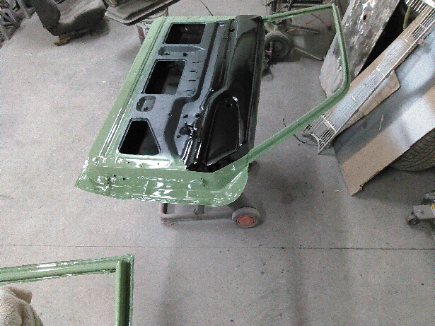 car door on a stand, being prepped for paint, with other car parts in background