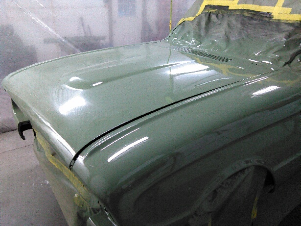 Car hood and fender covered in green paint, taped off for protection
