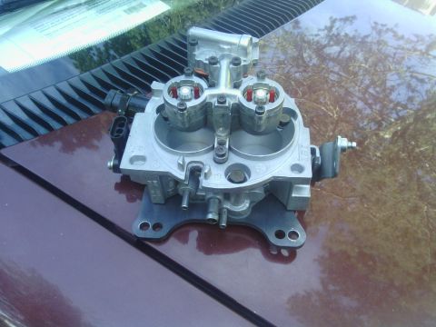 1978 Ford Bronco - Throttle body assembly, likely for a fuel-injected engine, resting on a car's hood.