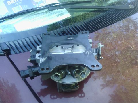 1978 Ford Bronco - A carburetor assembly is shown resting on the hood of a vehicle, with a manual and windshield wipers visible.