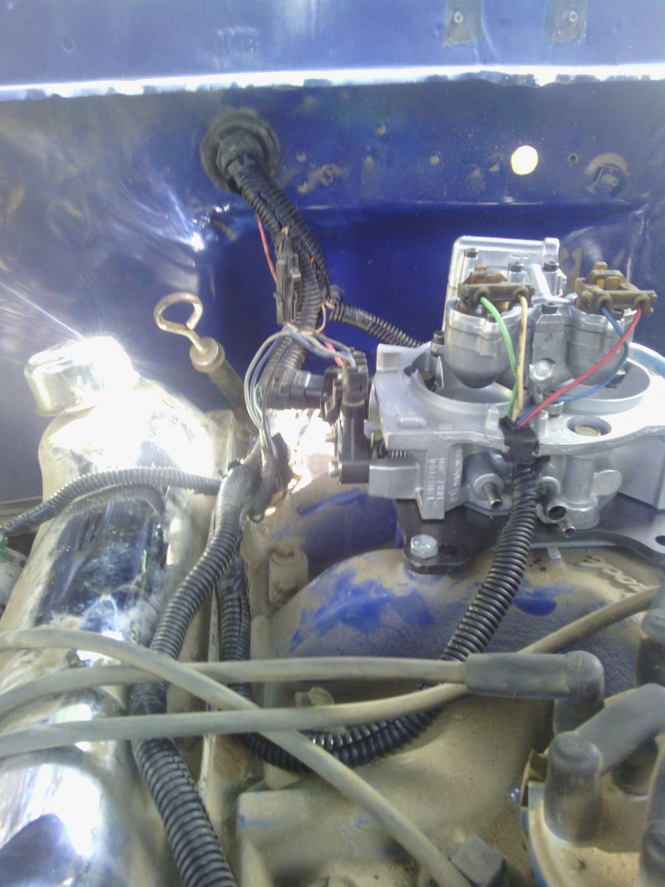 Close-up of engine carburetor and wiring harness with blue painted firewall in background