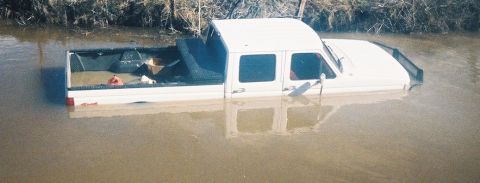 1991 Ford Bronco - A white four-door crew cab pickup truck submerged in muddy floodwater up to its doors, viewed from the side with the bed and cab visible ab…