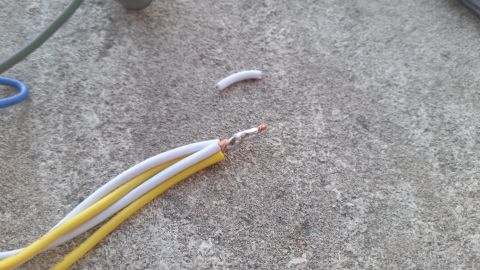 1985 Ford Bronco - Close-up of electrical wires with stripped ends and a piece of insulation lying on a textured concrete surface.