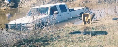 1991 Ford Bronco - A white/light-colored Ford crew cab pickup truck stuck in a muddy pond or flooded area, viewed from the side-front angle with water up to i…