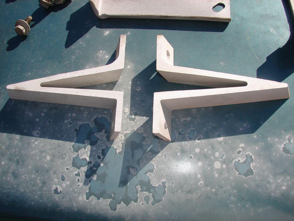 Several metal brackets and a bolt are laid out on a teal surface with peeling paint