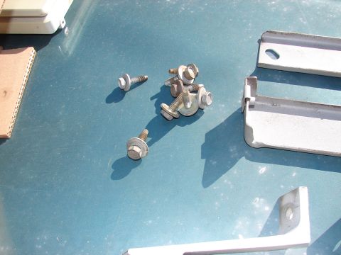 1973 Ford Ranchero - Several bolts and metal brackets are scattered on a blue surface, possibly a car hood or trunk.