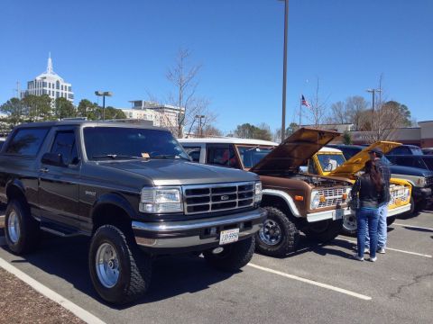 1979 Ford Bronco - Several Ford Broncos are parked in a lot on a sunny day, with two older models showing their engines.