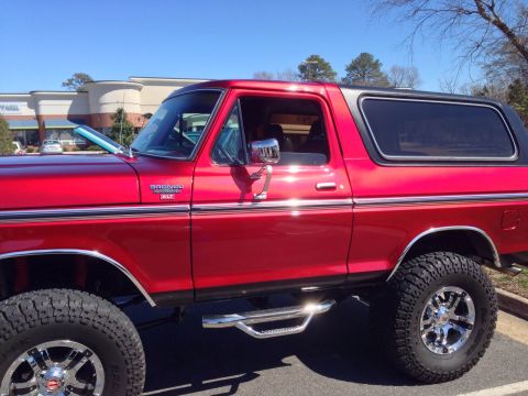 1979 Ford Bronco - This red 1979 Ford Bronco features chrome wheels and side steps, seen from the side.