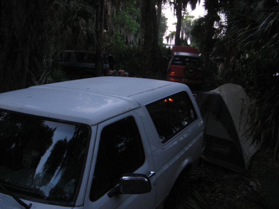 White SUV parked next to a tent, with another red SUV in the background