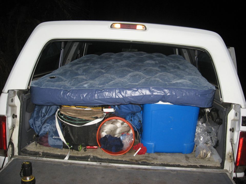 White pickup truck bed loaded with an air mattress, blue cooler, and various camping supplies