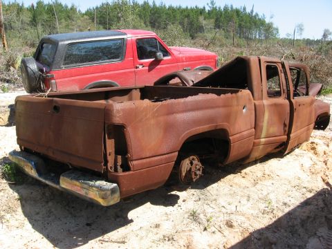 1994 Ford Bronco - A red 1994 Ford Bronco is parked behind a heavily rusted pickup truck in an outdoor setting.