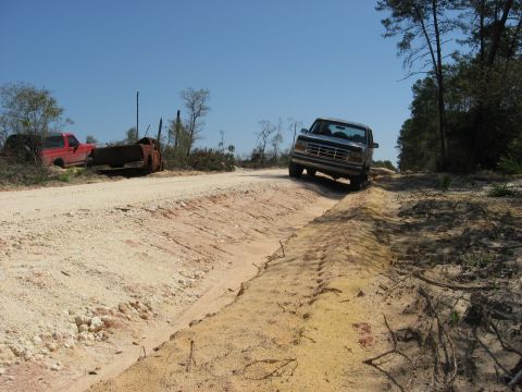 1994 Ford Bronco - A 1992 Ford Bronco navigates a rough dirt track, with abandoned trucks visible to the left.
