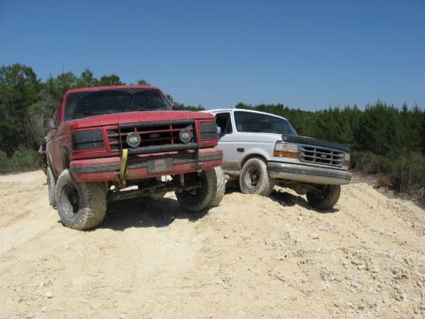 1994 Ford Bronco - Two Ford Broncos navigate a sandy incline under a clear blue sky.