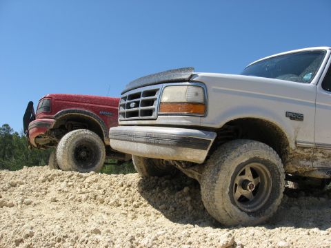 1994 Ford Bronco - Two Ford Broncos are shown off-road under a clear blue sky.