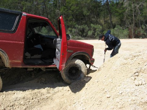 1994 Ford Bronco - A person digs dirt away from a red Ford Bronco that is stuck in a sandy area.