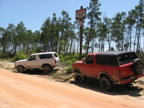 1994 Ford Bronco - Two Ford Broncos are parked off-road next to a sign warning of unexploded bombs.
