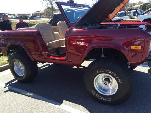 1979 Ford Bronco - A red convertible SUV with its hood open is parked on asphalt, showing its tan interior.
