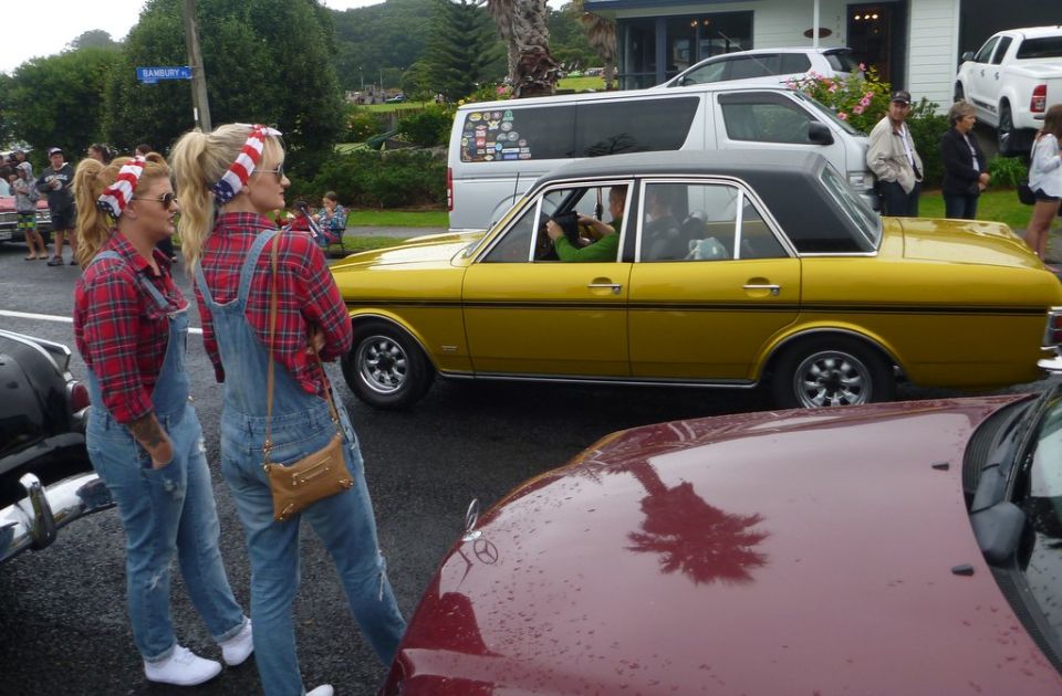 Yellow sedan with black vinyl roof and two women in overalls standing nearby