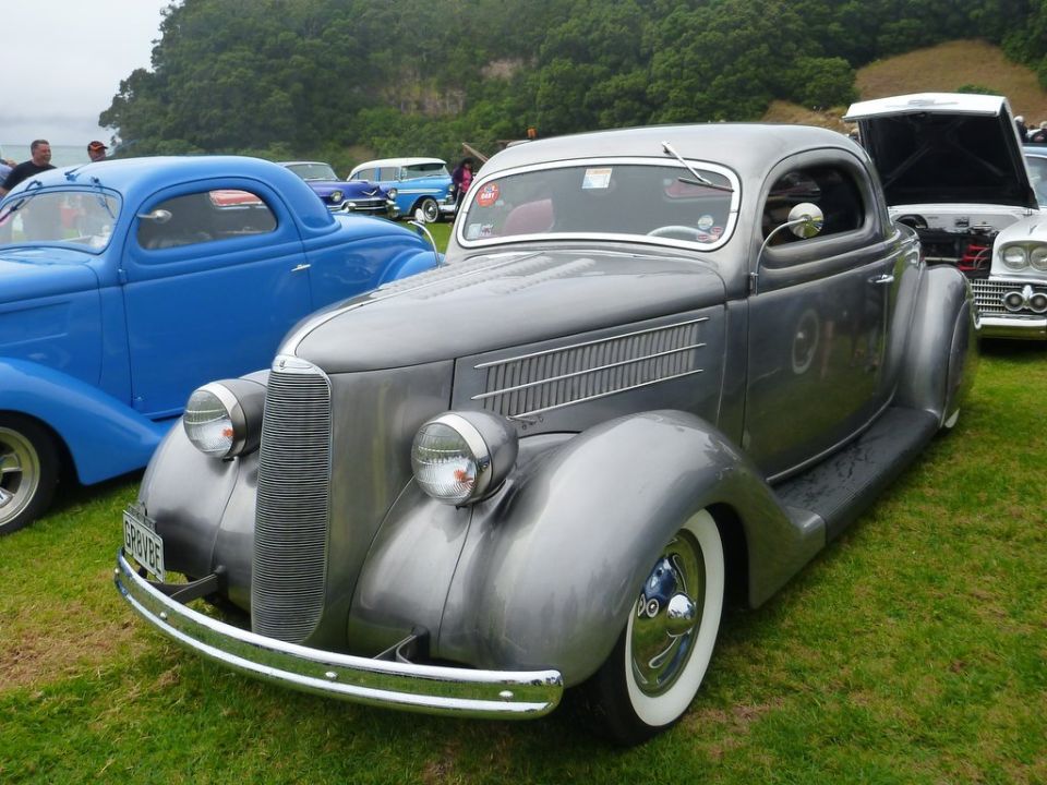 Gray 1935 Ford Coupe hot rod with whitewall tires parked on grass, blue coupe in background