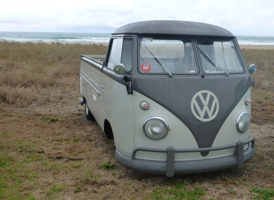 Two-tone Volkswagen Type 2 pickup truck parked on grassy area near beach